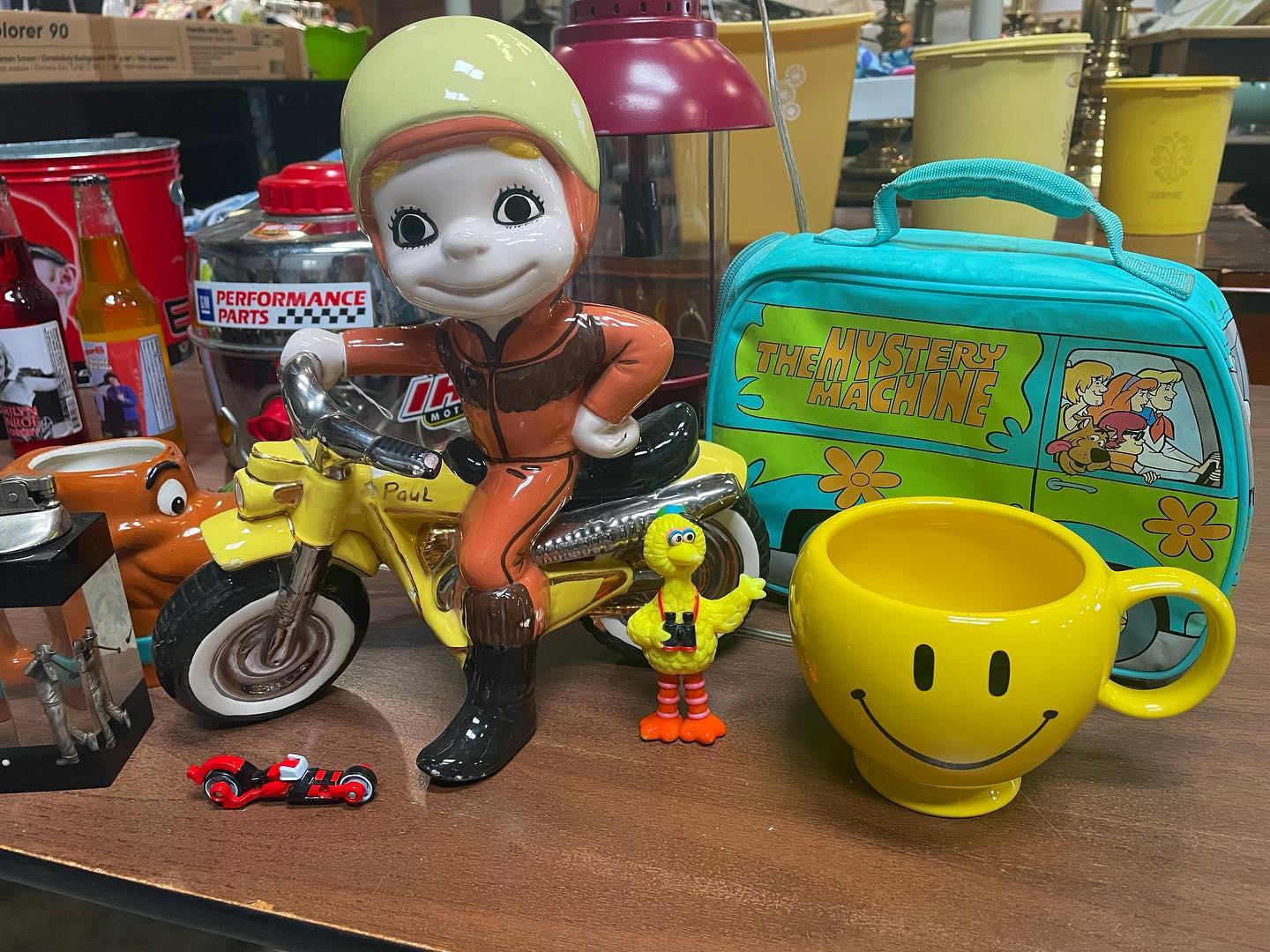 statues, a smily face mug, and scooby doo bag on a table
